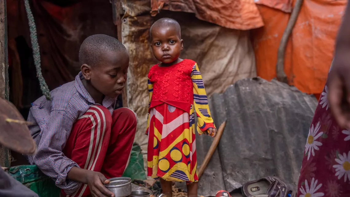 Una ni&ntilde;a juega con su hermano junto a su refugio en un campamento de desplazados internos situado en las afueras de Mogadiscio, en Somalia.