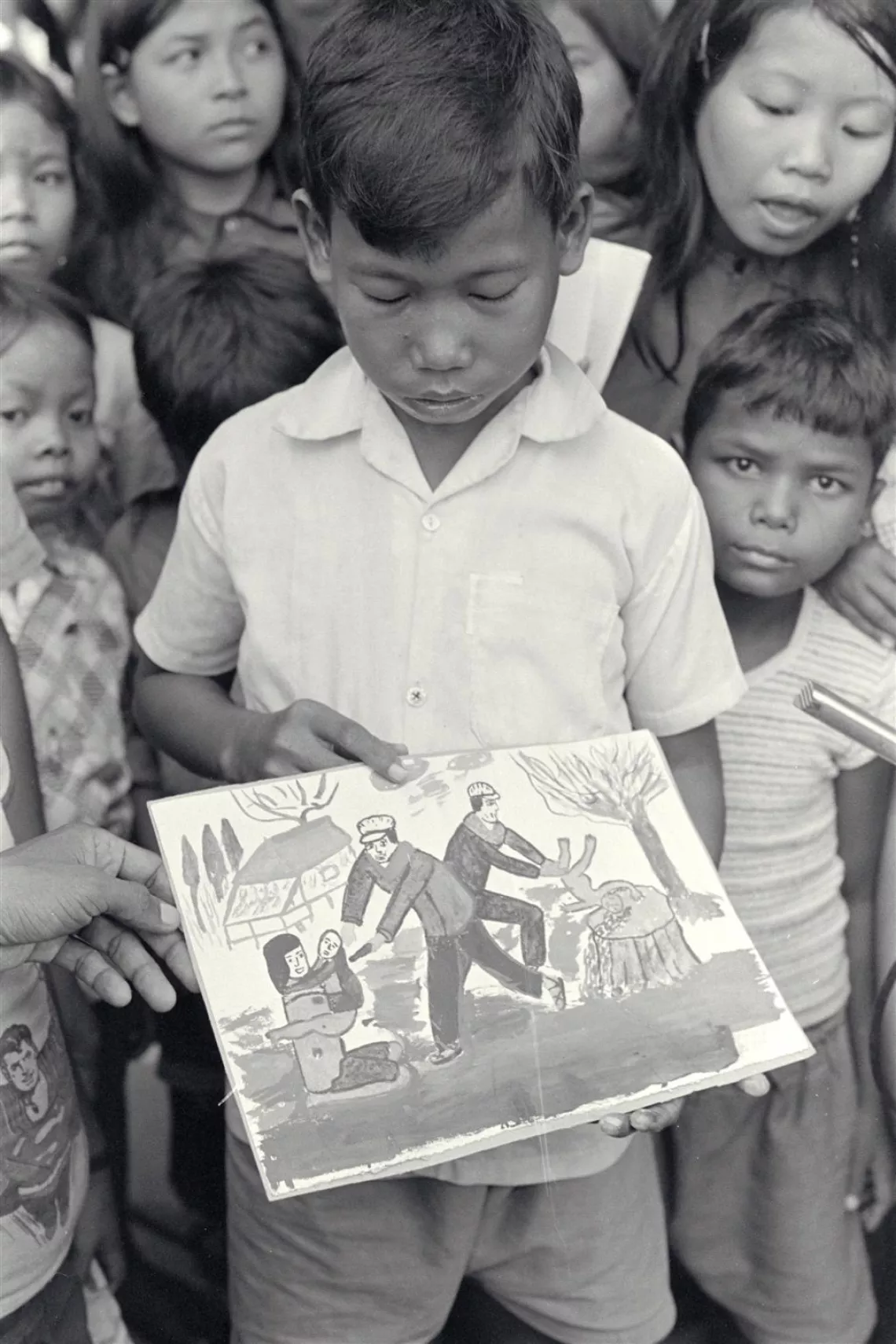 A boy holds a drawing showing the atrocities of the Khmer Rouge regime.