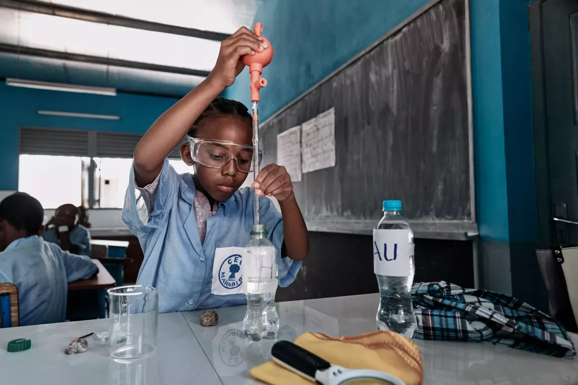 A child in a lab coat working on a science project at a table filled with materials and tools.