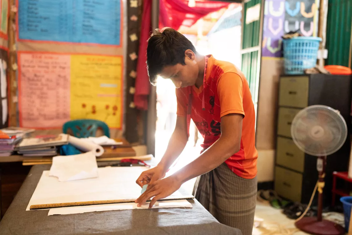 Bangladesh. Saiful Islam, 17, lines up a ruler on some paper at a tailoring workshop at a Multi-Purpose Centre in a Rohingya refugee camp in Cox&rsquo;s Bazar.