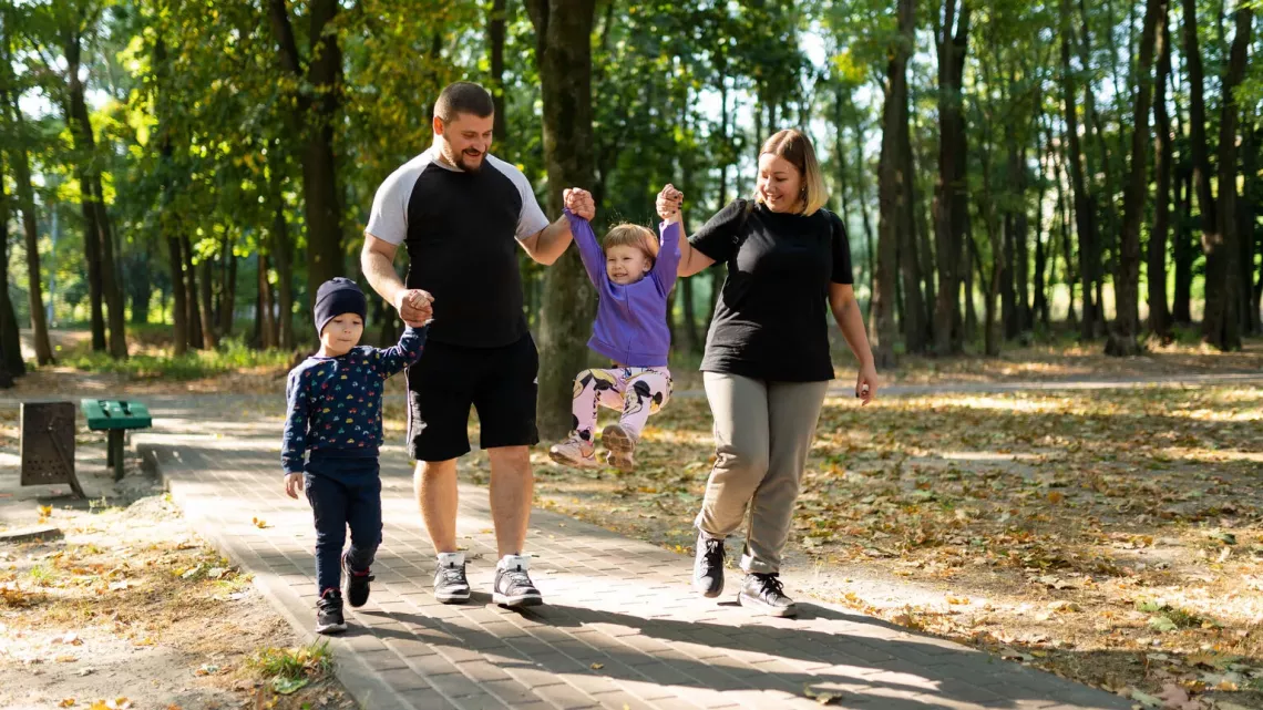 Liudmila and her husband swing their daughter, Veronika, while her twin brother, Tymur, walks beside them during a walk in a park in Kyiv, Ukraine. 