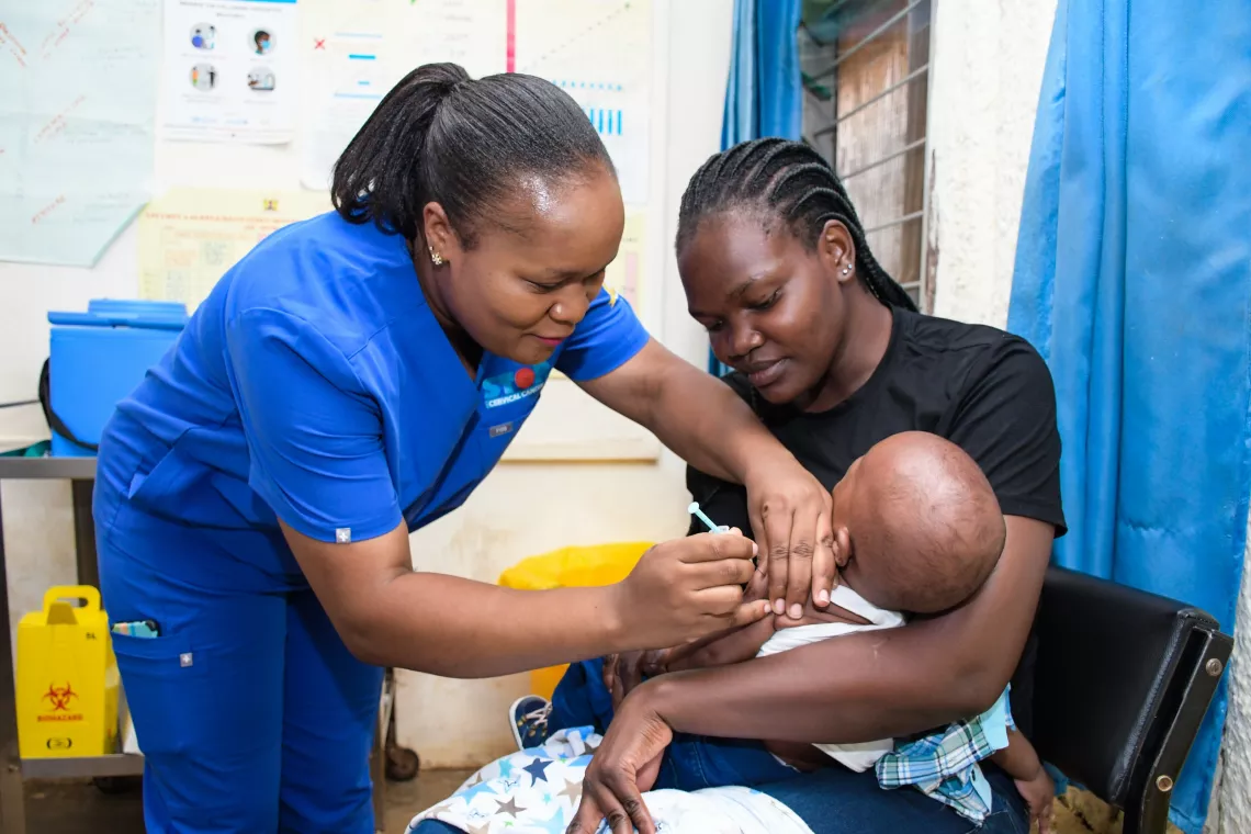 6-month-old baby is held by his mother while being vaccinated against malaria by health worker.