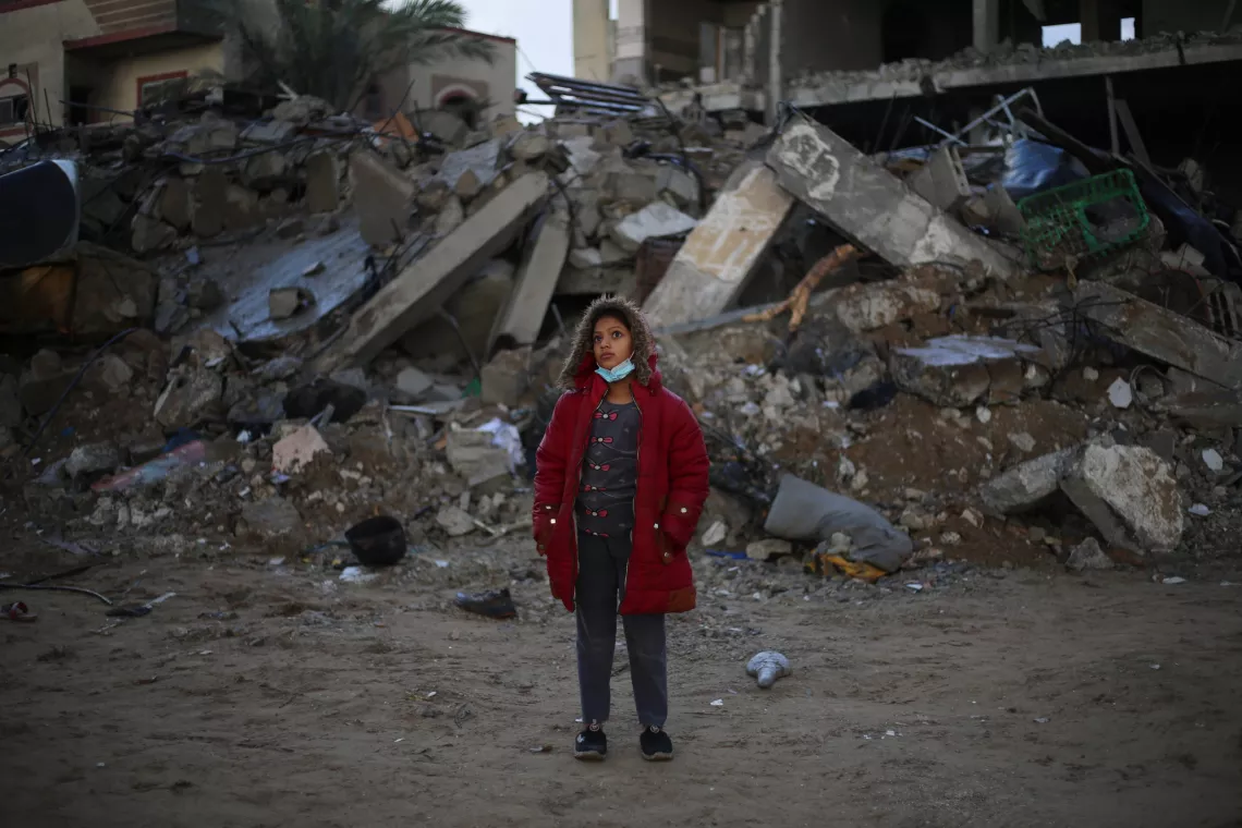 An adolescent girl stands in front of a ruined building, Gaza