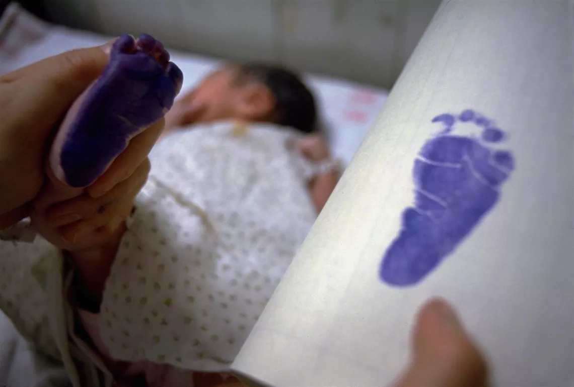 A baby's footprint is taken on a piece of paper with purple ink.