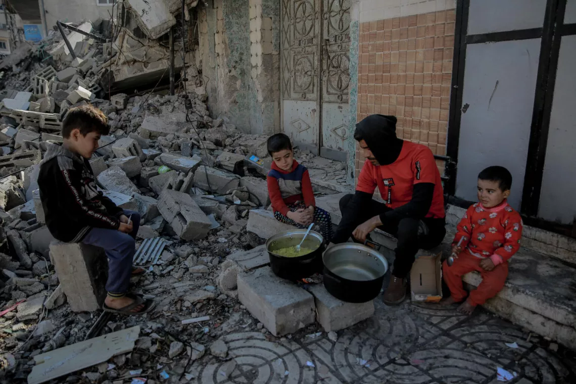 35岁的哈勒德在加沙城西部al-Rimal社区被毁的家前，孩子们围坐在他身边，由于天然气短缺，他在柴火上做饭。
