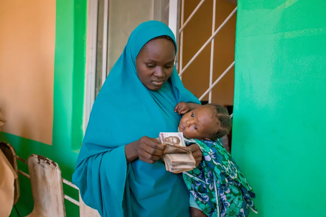 Khadija Usaini, a 20-year-old taking care of Usaina Isah, is checking her funds during the Cash Transfer disbursement at Jikamshi Facility in Katsina State.