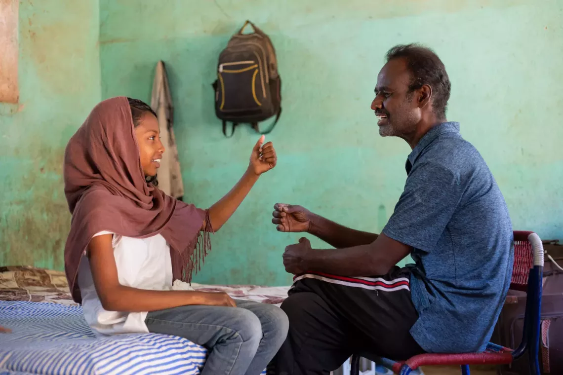 In Sudan, 11-year-old Samar pretends to play a violin as her father, Nassir, sings along. Displaced from Khartoum, they are now staying in a classroom at a primary school in Kassala state. 