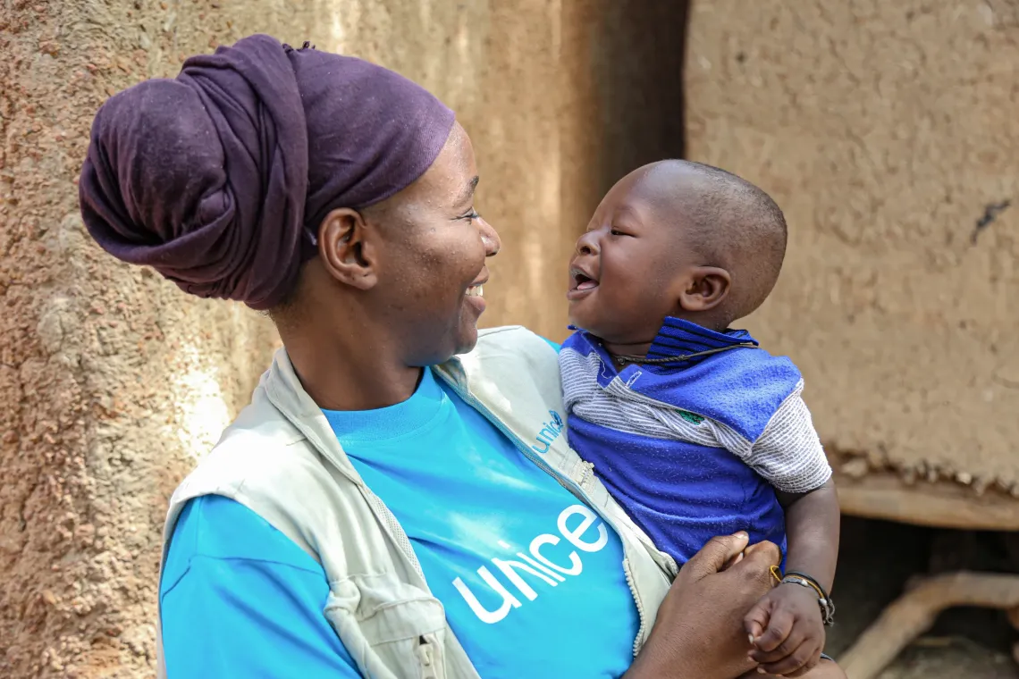 A UNICEF staff member smiles while holding a laughing baby.