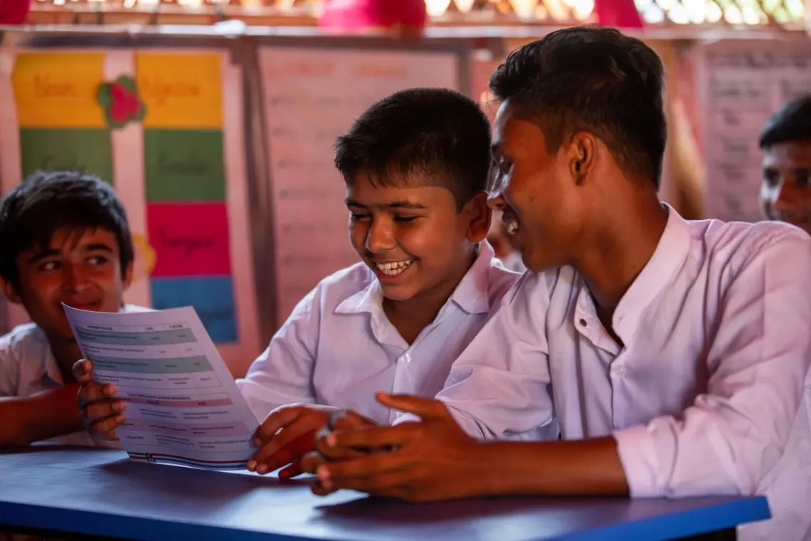 Bangladesh. Three boys look at a report card in a class room in a camp in Cox's Bazar.