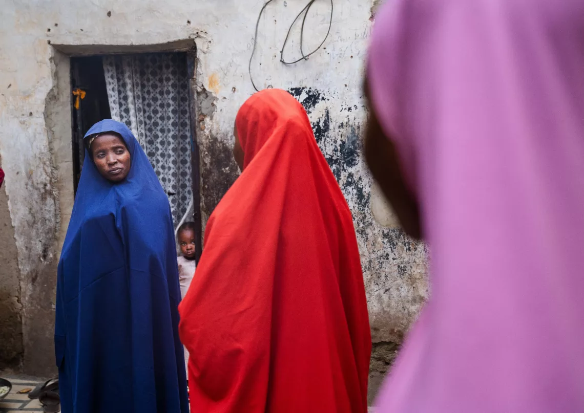 Nafisa Ibrahim, 5, rear, peaks out as her mother, Hadize Ibrahim, 35, left, speaks with Volunteer Community Mobilizer (VCM), Shamsiyya Abdullahi Jariri, 30, middle, accompanied by her sister, Hadiza Abdullahi Jariri, 25, right, about the week-long second phase of the single-dose human papillomavirus (HPV) vaccine rollout, targeting girls aged 9-14 years, in Katsina, Nigeria, on 30 May 2024.