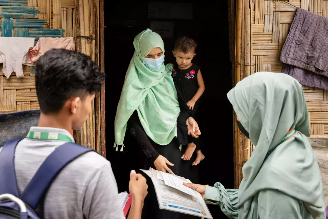 Bangladesh. Two nutrition volunteers walk speak to a woman holding her child outside her shelter.
