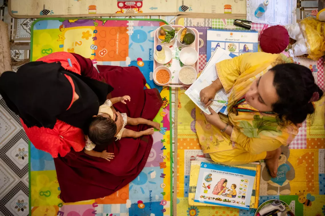 Bangladesh. A mother sits on the floor with her child on her lap while she attends a nutrition session.
