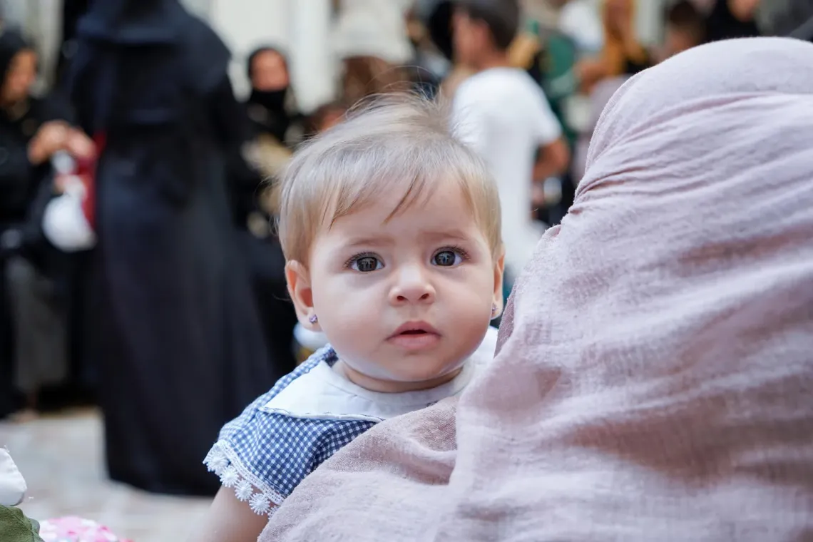 Syria. A baby looks over her mother's shoulder mother as they wait for a medical checkup at a UNICEF-supported clinic.