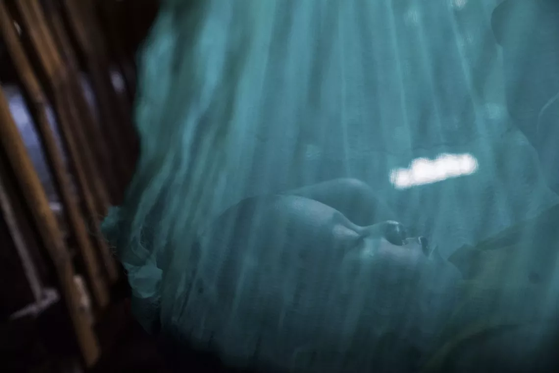 An infant sleeps on a cot shrouded by a green mosquito net