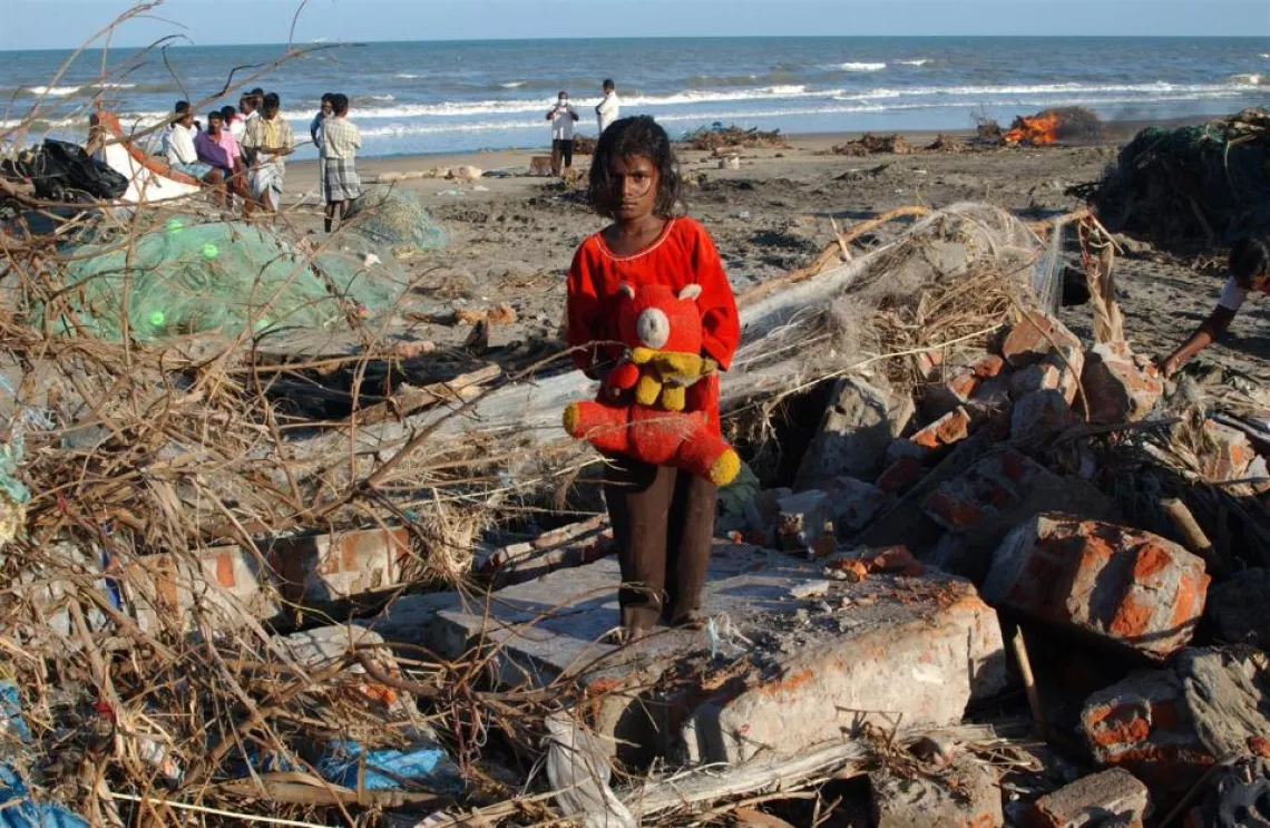 An eight-year-old child stands on what remains of her home following a tsunami. India 2005.