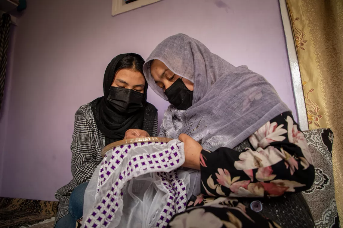 A mother and daughter look with heads bended towards each other at the embroidery that mother is busy with.