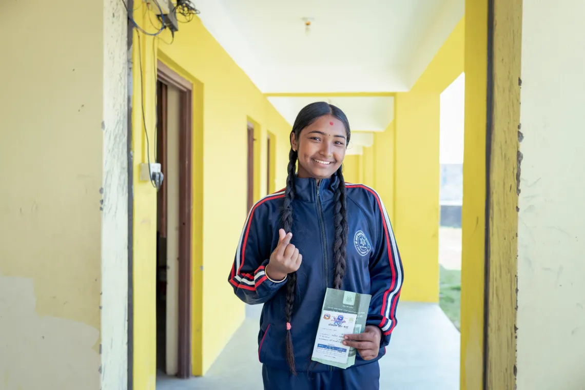 A teenage girl smiles and holds her fingers up to shape a heart.