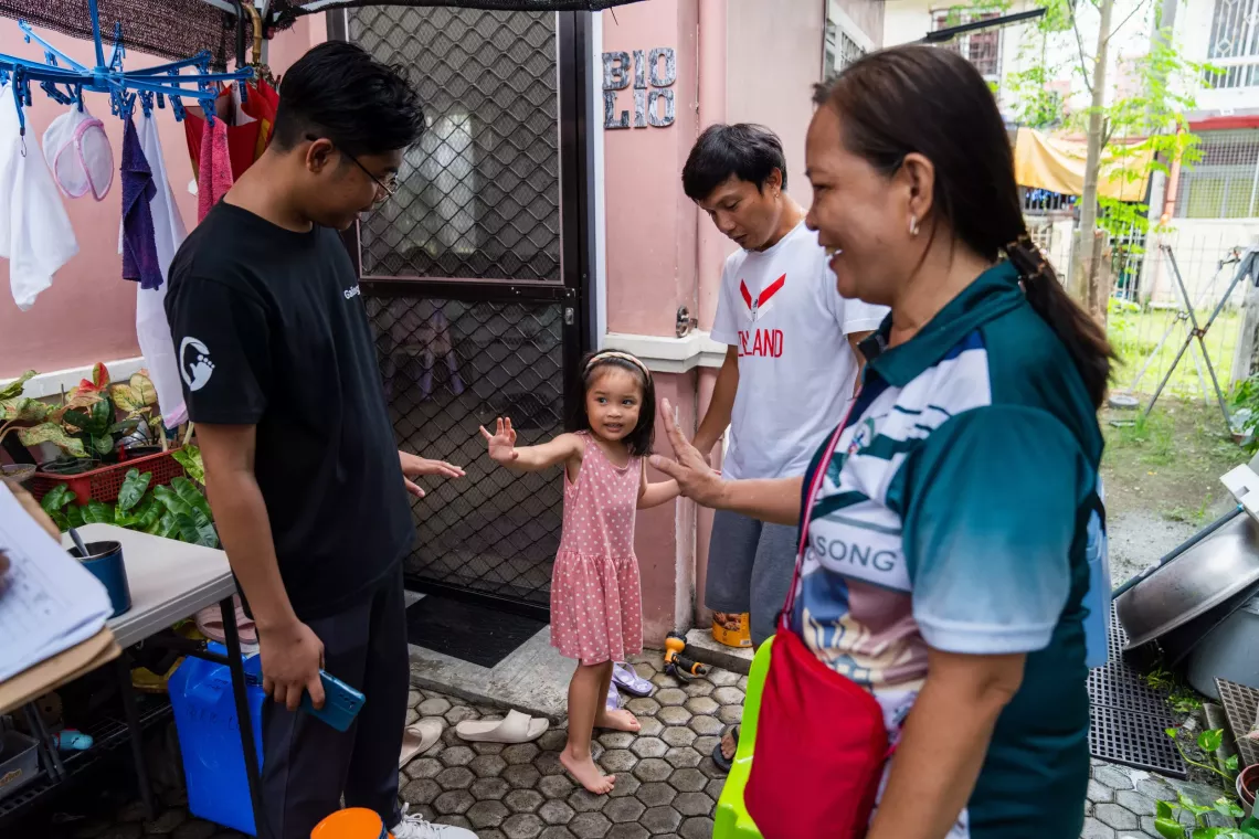 A youth mobilizer. and health worker are greeted by a small girl and her father while going door-to-door to offer vaccinations