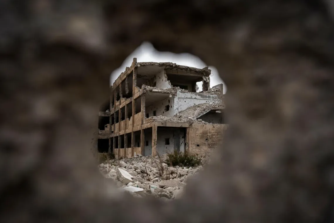Syria. A damaged school building is seen through a hole in a wall in Homs.
