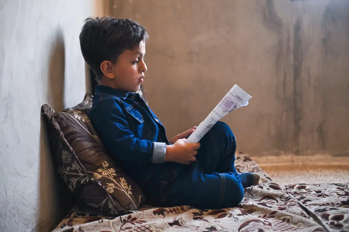 Syria. A boy sits on the floor reading at his home in Zabadin, Rural Damascus.