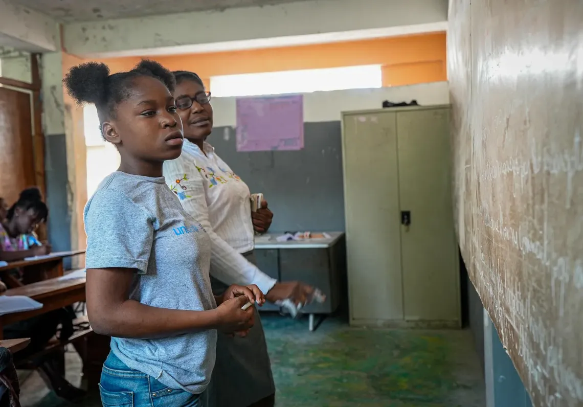 Haiti. A girl stands looking at a chalkboard with her teacher.
