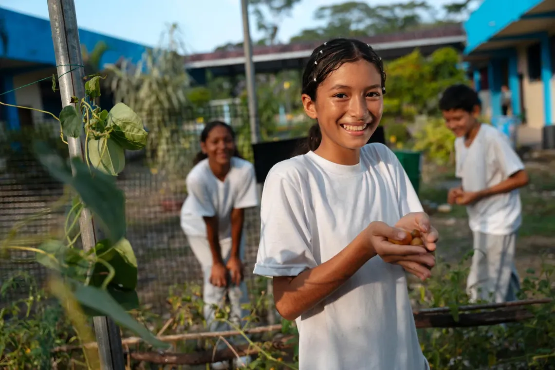 A girl hold up produce from the garden at her school in Ecuador.