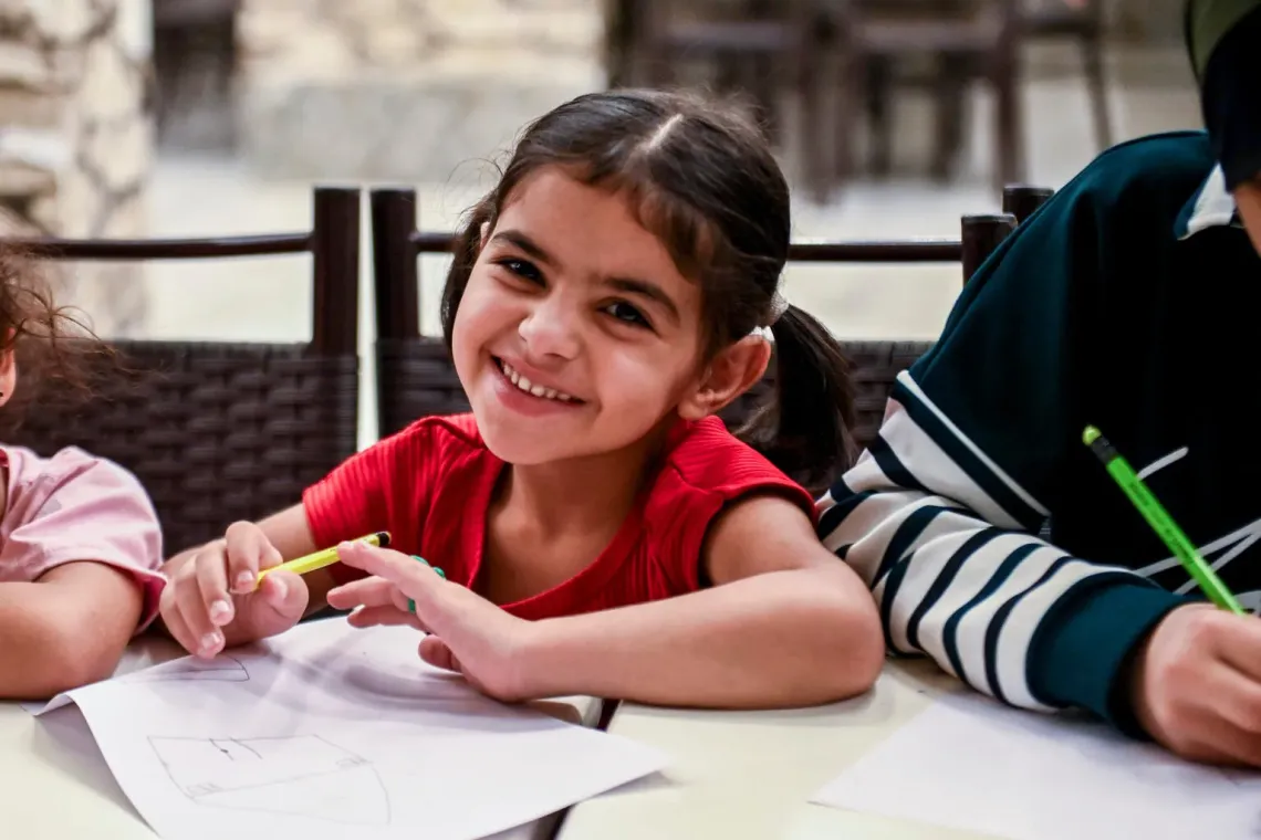 A young girl smiles as she works on a drawing.