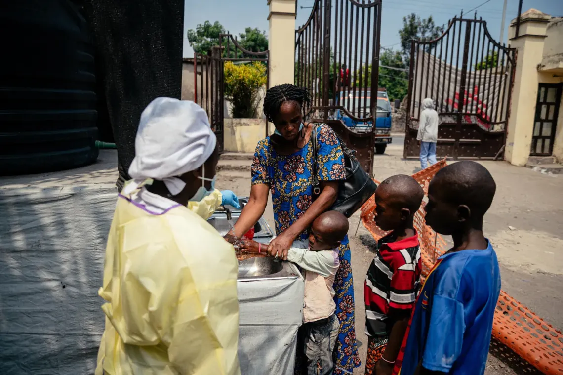 Democratic Republic of the Congo. A mother helps her children wash their hands at a visitor handwashing and temperature screening checkpoint at Kyeshero Hospital in Goma.