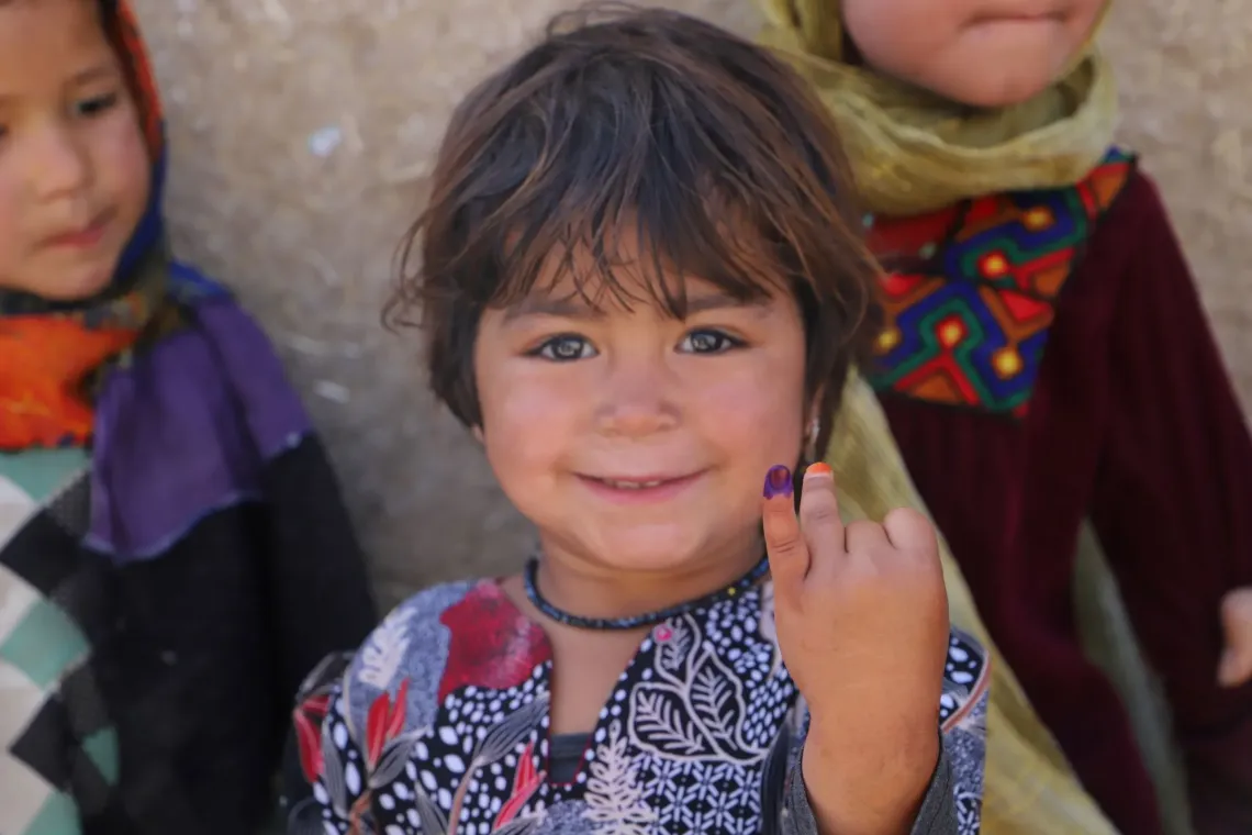 Une enfant souriante aux cheveux courts et fonc&eacute;s montre son doigt marqu&eacute; d&rsquo;encre violette apr&egrave;s avoir re&ccedil;u un vaccin contre la polio.