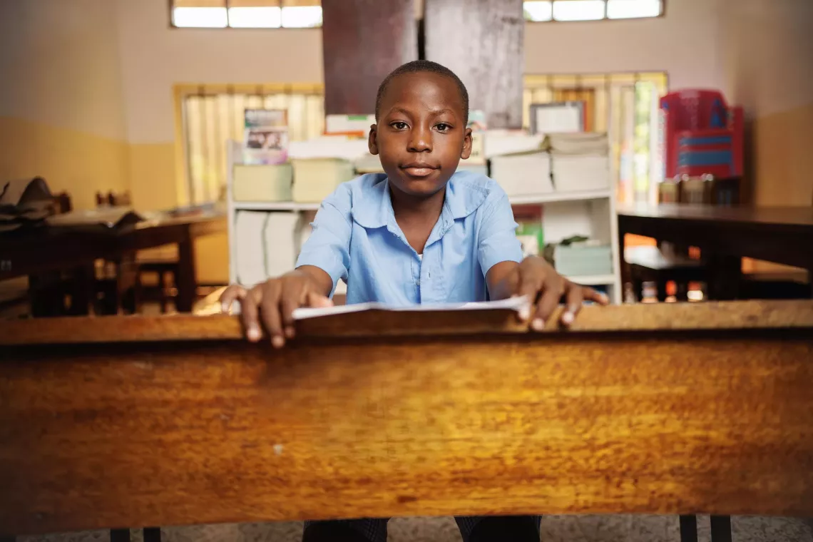 A boy sits at a desk leaning over his letter to adults.