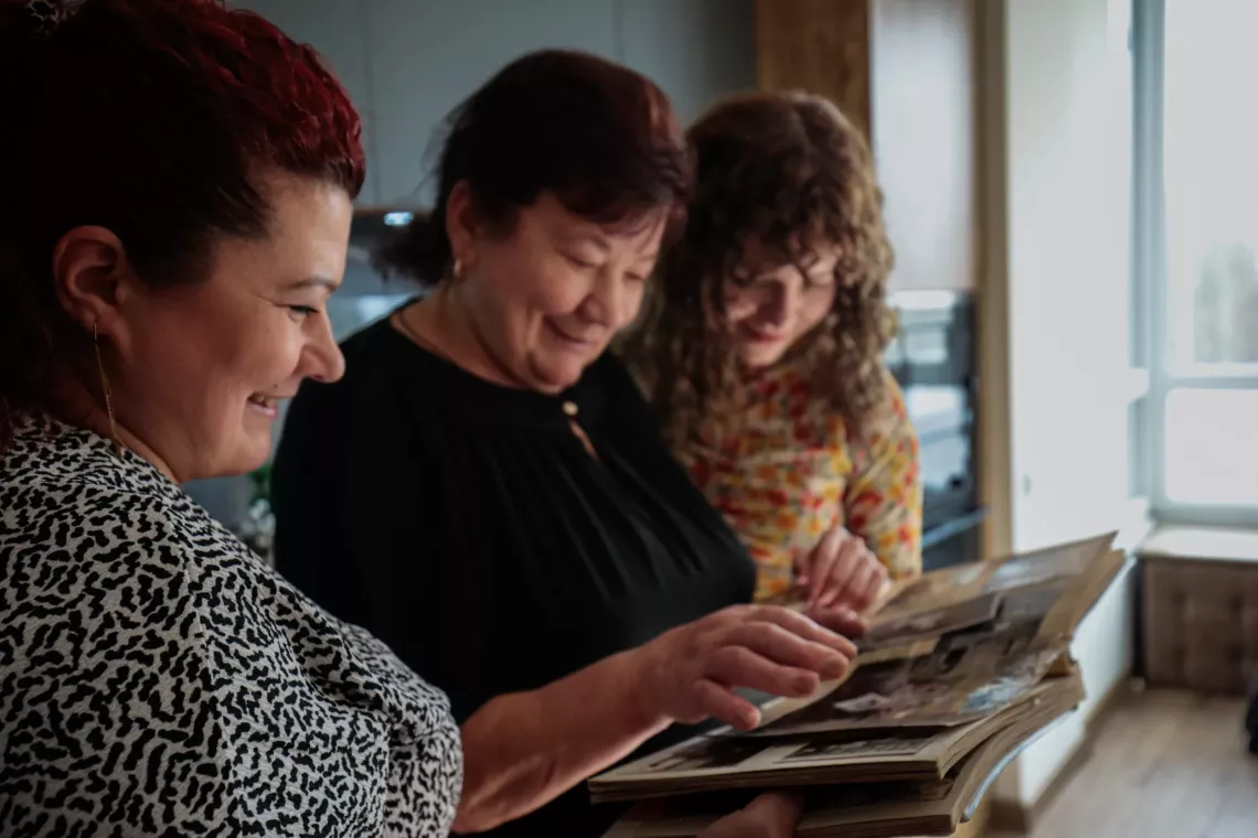 A 15 year old girl looks at photos in a family photo album with her mother and grandmother.