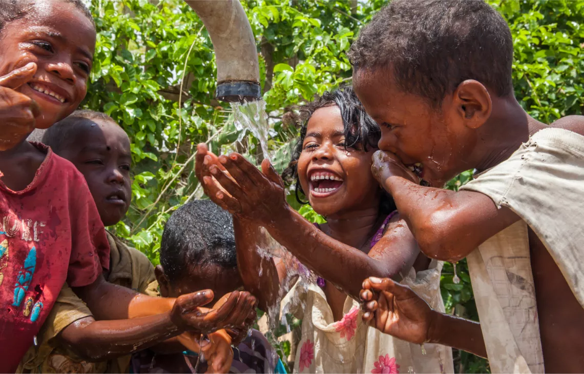 Happy children getting water from a pipe.