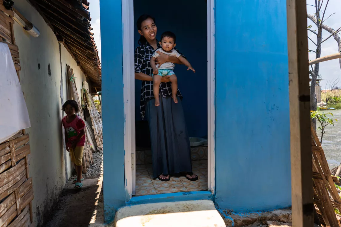 sanitation in indonesia: woman holding a child exiting a communal toilet