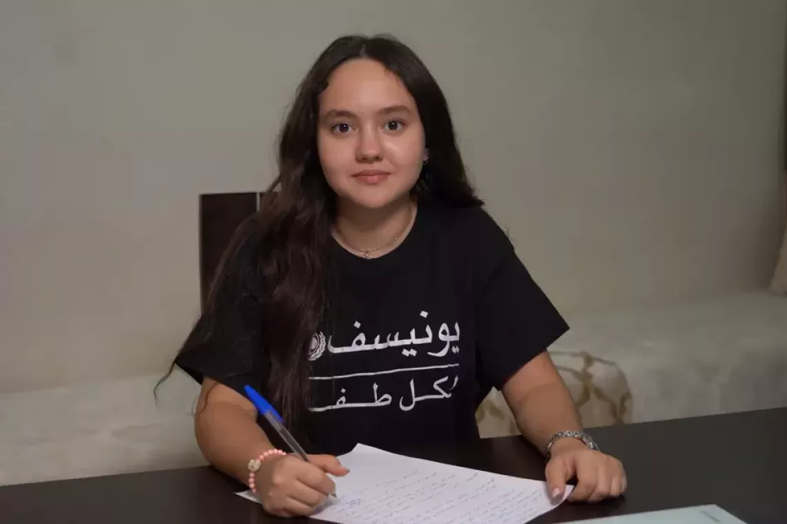 A girl in Morocco sits at a desk writing a letter.