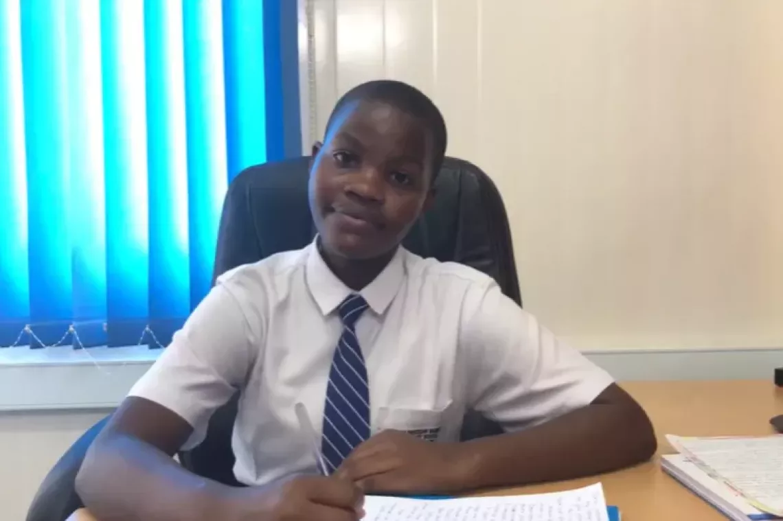 A boy in a shirt and tie sits at a desk.