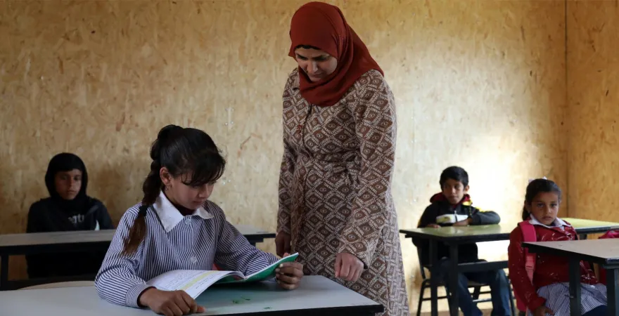 A teacher stands next to a child at a school desk