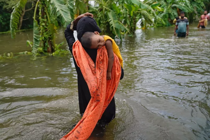 A mother carrying her child through the flood water in Feni, Bangladesh. August 2024