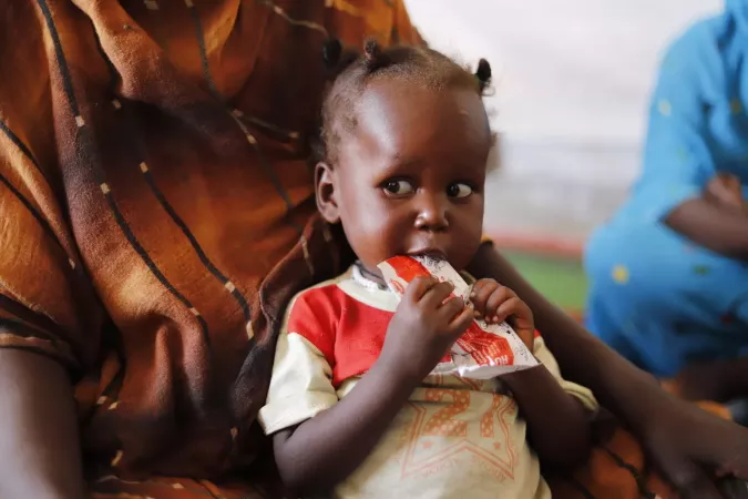 On 4 May, a child suffering from malnutrition eats ready-to-use-therapeutic-food at a UNICEF-supported Primary Health Clinic in Tawila, North Darfur. The attacks on Zamzam and Abu Shouk and other IDP camps have forced an estimated 400,000 to 450,000 people towards Tawila, the areas surrounding Jebel Marra, and beyond. The families arrive with little or nothing: no food, no shelter, and lacking the basic necessities for survival.