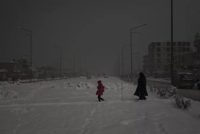 A woman and child walk on snow on a hazy day in Afghanistan