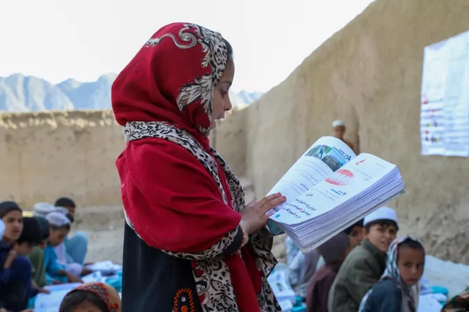A 5 years girl stand to read the book while others listen to her 