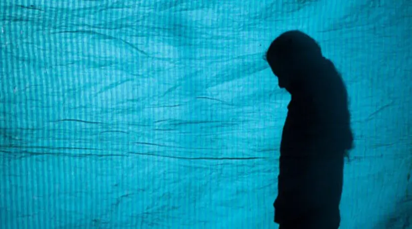 Silueta de una ni&ntilde;a cabizbaja frente a un fondo azul.