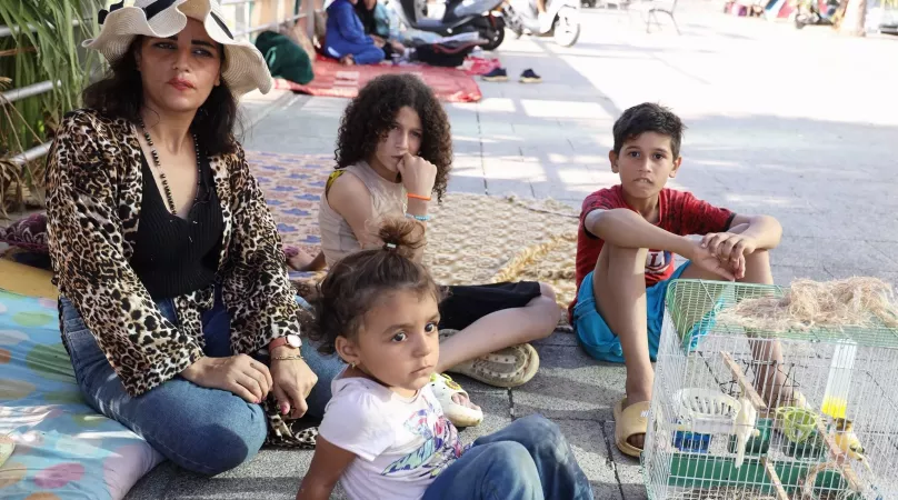 Lebanon. A woman sits on a sidewalk with her family.