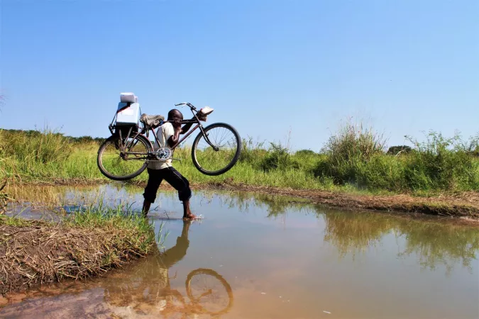 Man carries a bicycle across a river