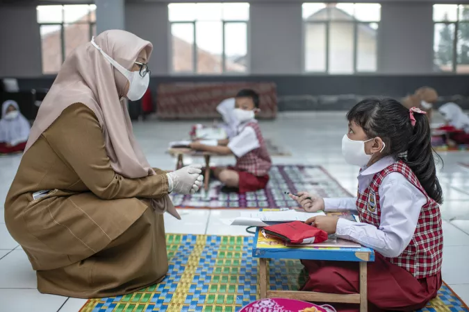 A student and teacher sit on the floor together.