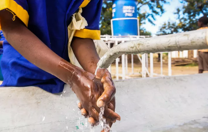 A person washes their hand with soap and water from a tap.