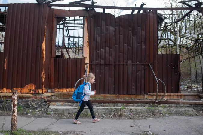 Ukraine. A girl walks past a destroyed building.