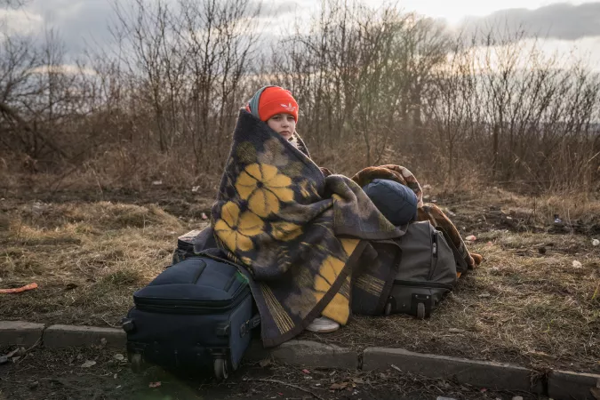 Ukraine. A girl wrapped in a blanket sits by the road near the Ukraine border.