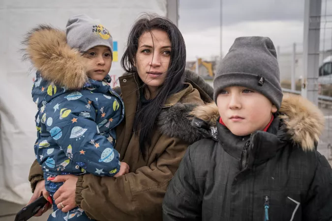 Romania. A woman stands near a Blue Dot tent with her two children.