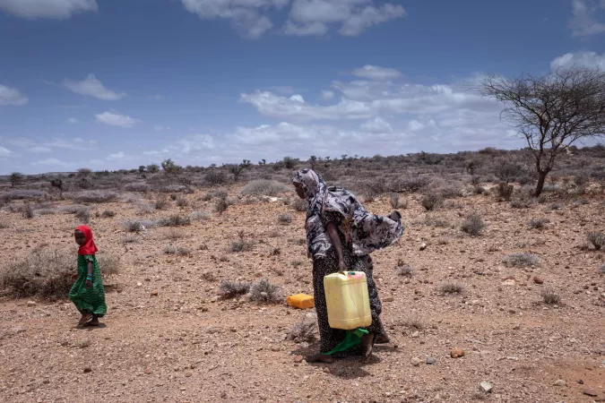 A woman and girl carry water jugs through the desert. 