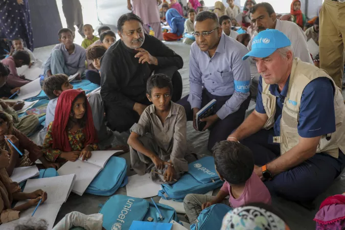 Children and adults sit in a circle in a tent.